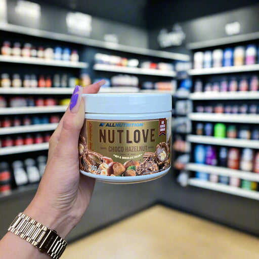 Close-up of (Allnutrition Nutlove 500g) held up inside My Supplement Shop, clearly showing the front label in a Sports Nutrition setting.
