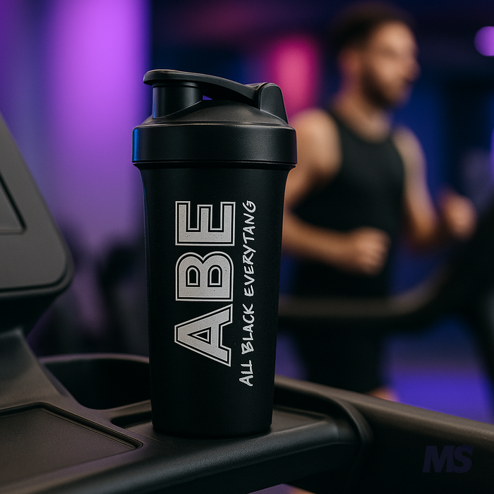 The shaker sitting in the cup holder of a treadmill, spin bike, or weight bench, gym-goer in the background