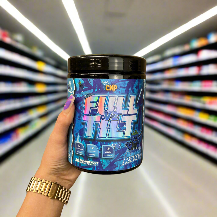Close-up of (CNP Full Tilt V2 570g) held up inside My Supplement Shop, clearly showing the front label in a Sports Nutrition setting.