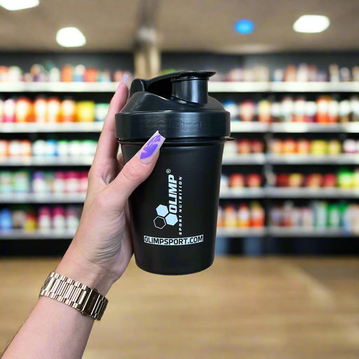 Close-up of (Olimp Sport Nutrition Shaker 600ml) held up inside My Supplement Shop, clearly showing the front label in a Sports Nutrition setting.